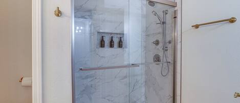 A glass-enclosed shower with a marble wall, a glass door, and a gold handle.