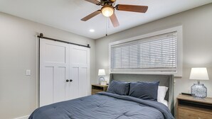 A bedroom with a bed, nightstands, a ceiling fan, a window with blinds, and a door.