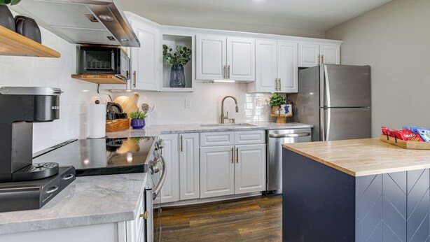 A modern kitchen with white cabinets, stainless steel appliances, and a wooden countertop.