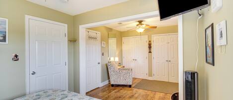 Un dormitorio con cama, ventilador de techo, televisor y una puerta que da a otra habitación.