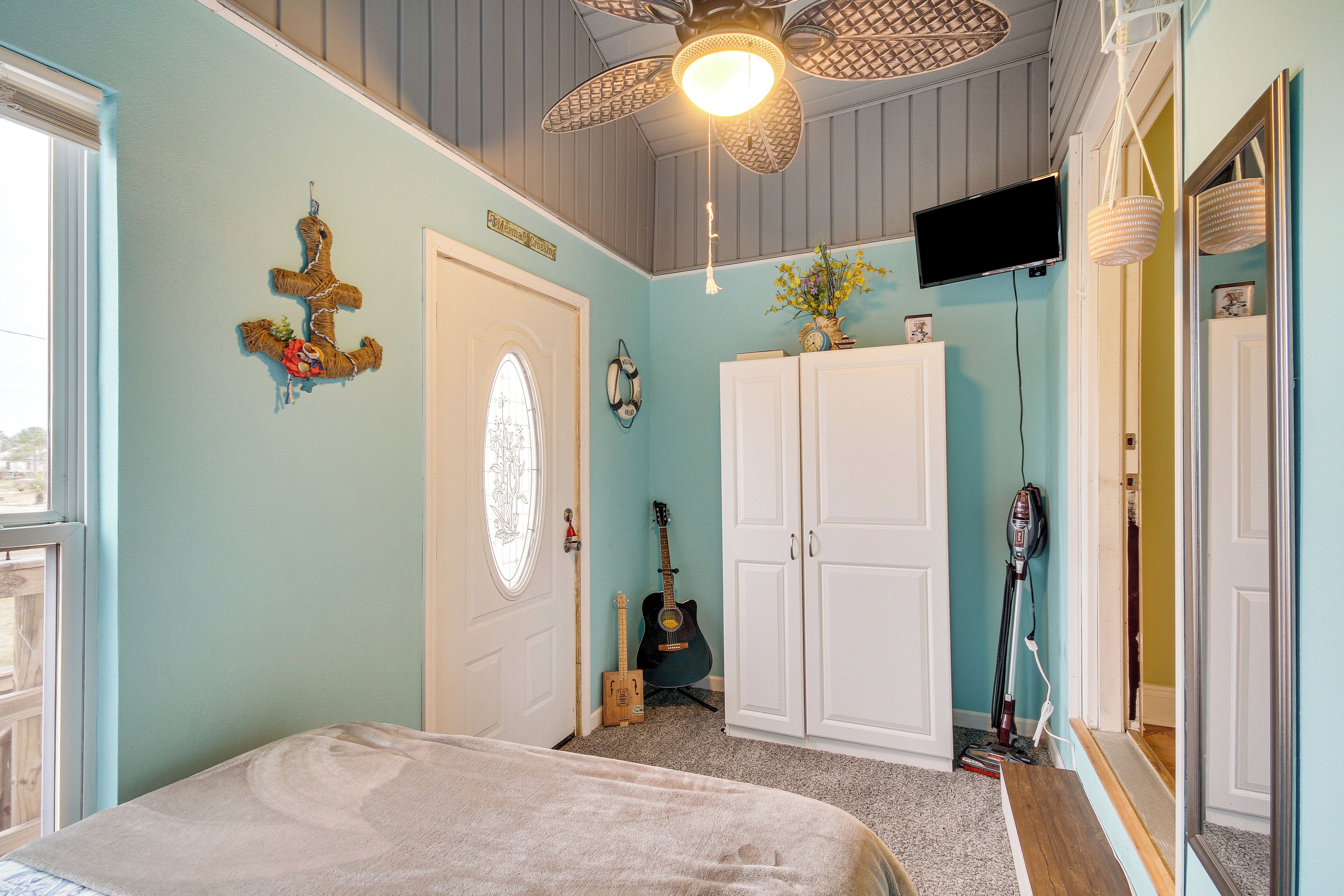 A bedroom with a bed, a guitar, a vacuum cleaner, and a TV on the wall.