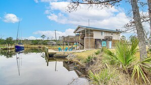A house with a dock extending into a calm body of water, surrounded by greenery and a clear sky. - Waterfront Bay St Louis Home w/ Private Dock! (Bay St Louis)