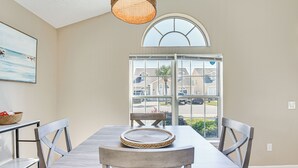 Een eethoek met een houten tafel en stoelen, een geweven placemat, een mandje op een bijzettafeltje en uitzicht door een groot raam.