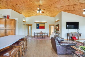 A spacious living area with a wooden ceiling, a dining table with chairs, a leather sofa, and a flat-screen TV mounted on the wall. - Private Yard & Fishing Dock: Canyon Rim Retreat (Amarillo)