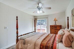 Quarto com cama, ventoinha no teto, cômoda e janela com cortinas.