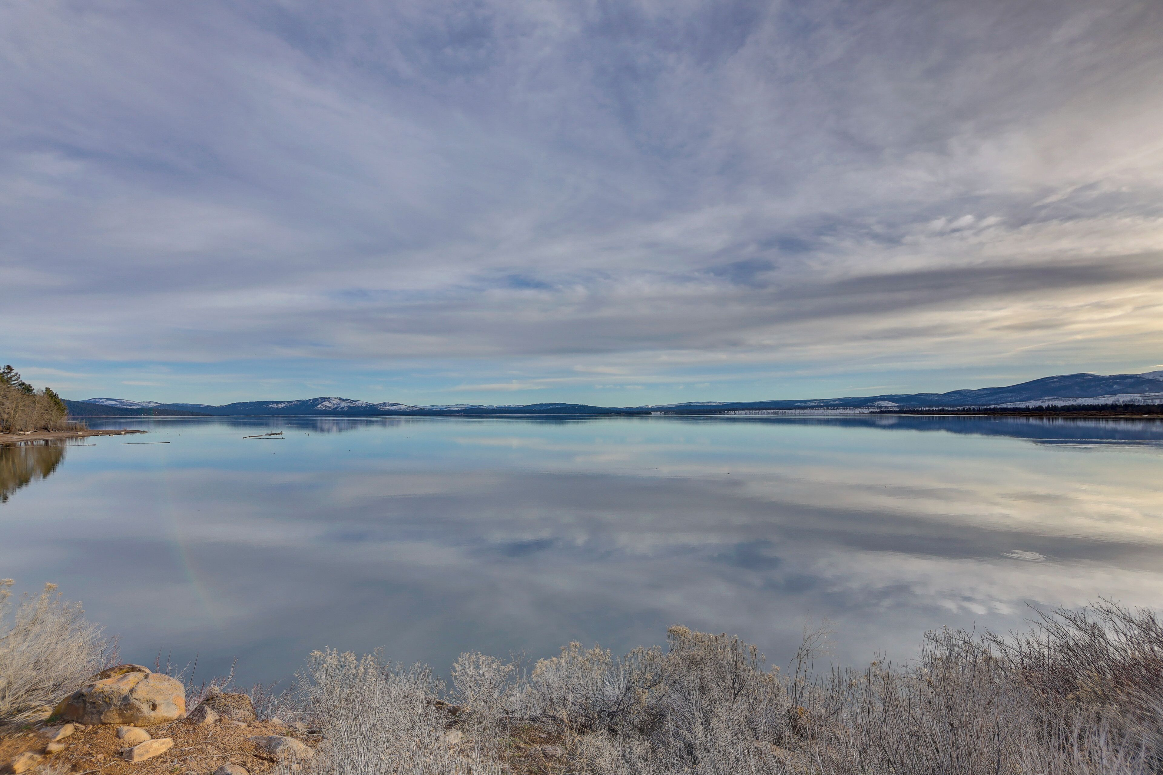 Ein ruhiger See mit Bergen im Hintergrund und blauem Himmel.
