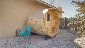 Una estructura cilíndrica de madera con una puerta, un área de estar cubierta con sillas y un suelo de grava.