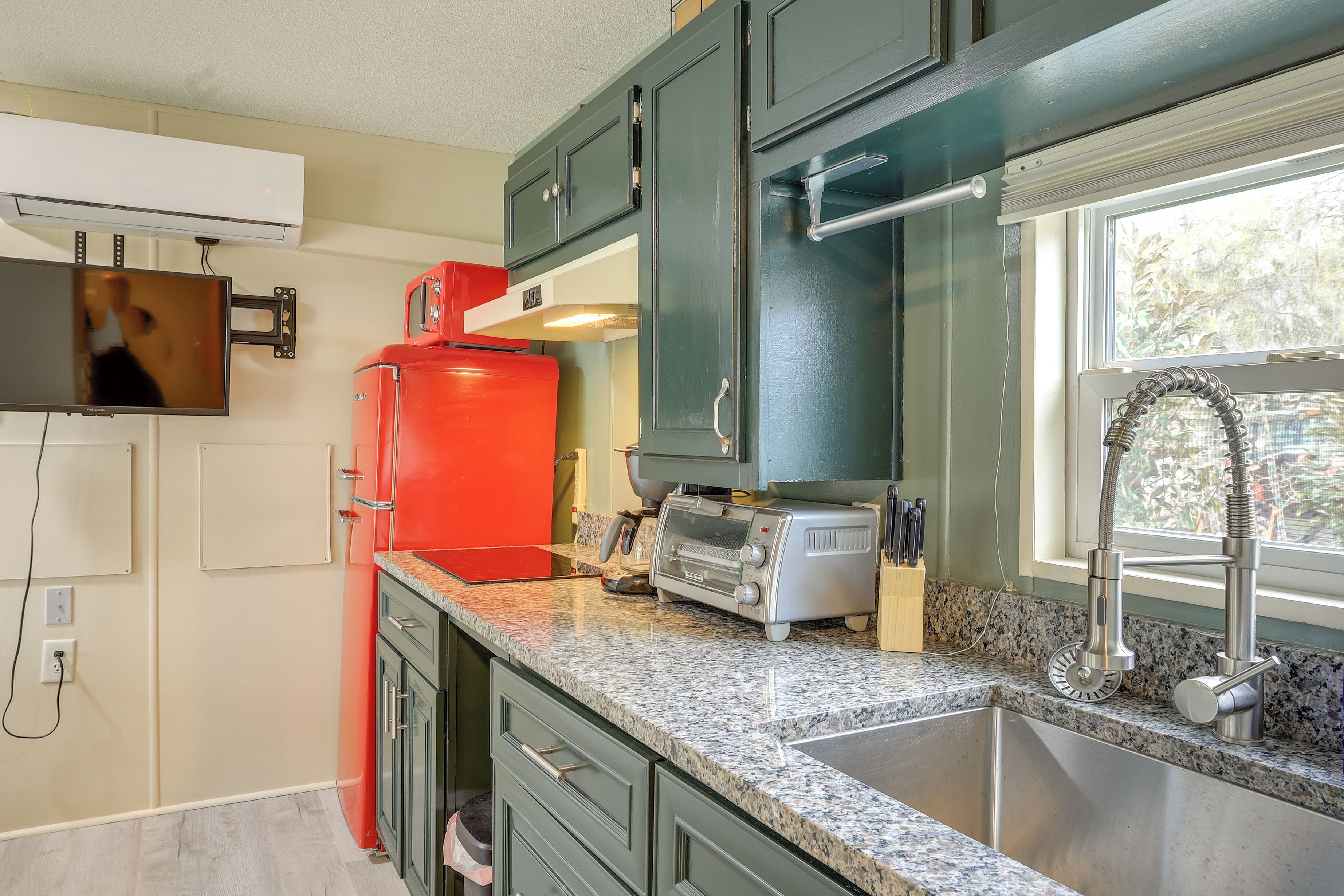 A kitchen with green cabinets, a red refrigerator, a toaster, and a sink with a modern faucet.