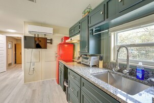 Una cocina moderna con gabinetes verdes, un refrigerador rojo, un horno empotrado y un ventanal con vistas a árboles.