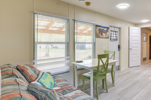 A room with a sofa, a table, and a chair. There are windows with blinds, a door, and a wall with a zebra painting. - Morriston Getaway w/ Patio - Near Hits Farm! (Morriston)