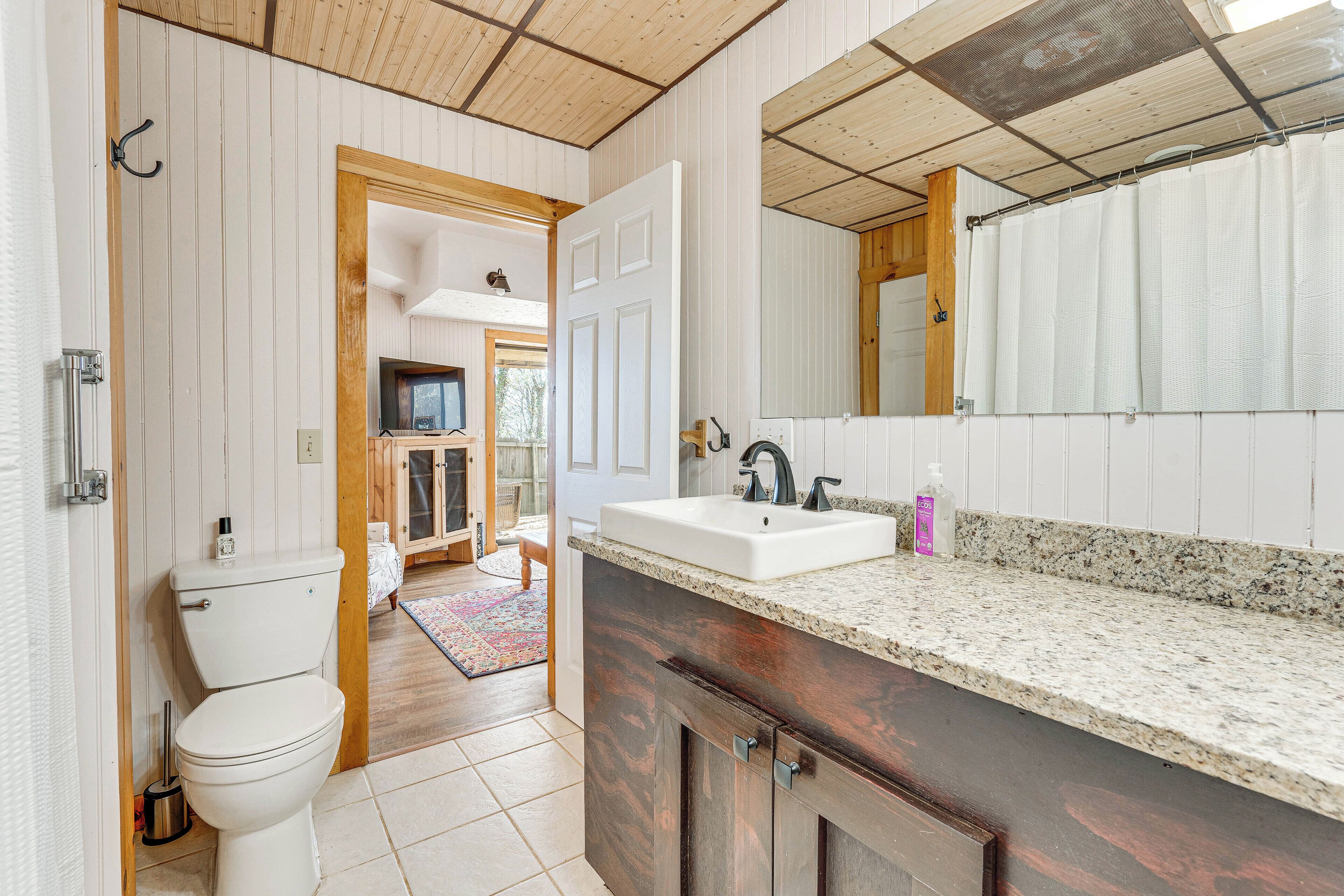 A bathroom with a white toilet, a sink with a granite countertop, and a wooden vanity.