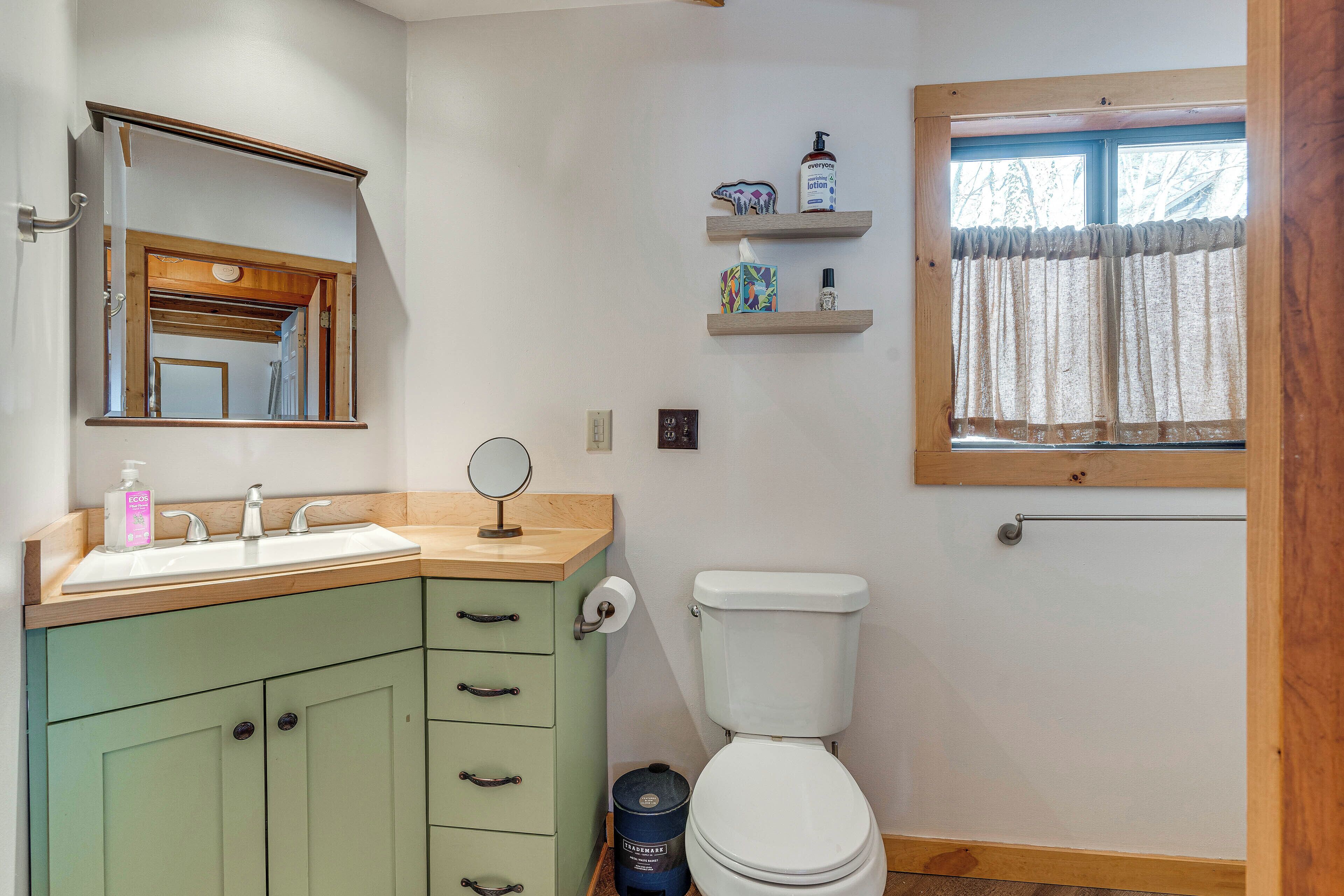A bathroom with a sink, mirror, toilet, and shelves with toiletries.