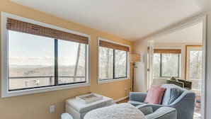 A living room with large windows, a grey sofa, a white pouf, and a wooden floor. - Mountaintop Blue Ridge Cabin: 2 Mi to Downtown (Blue Ridge)