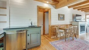 A compact kitchen with a built-in dishwasher, wooden ceiling beams, and a dining area with a patterned rug. - Mountaintop Blue Ridge Cabin: 2 Mi to Downtown (Blue Ridge)
