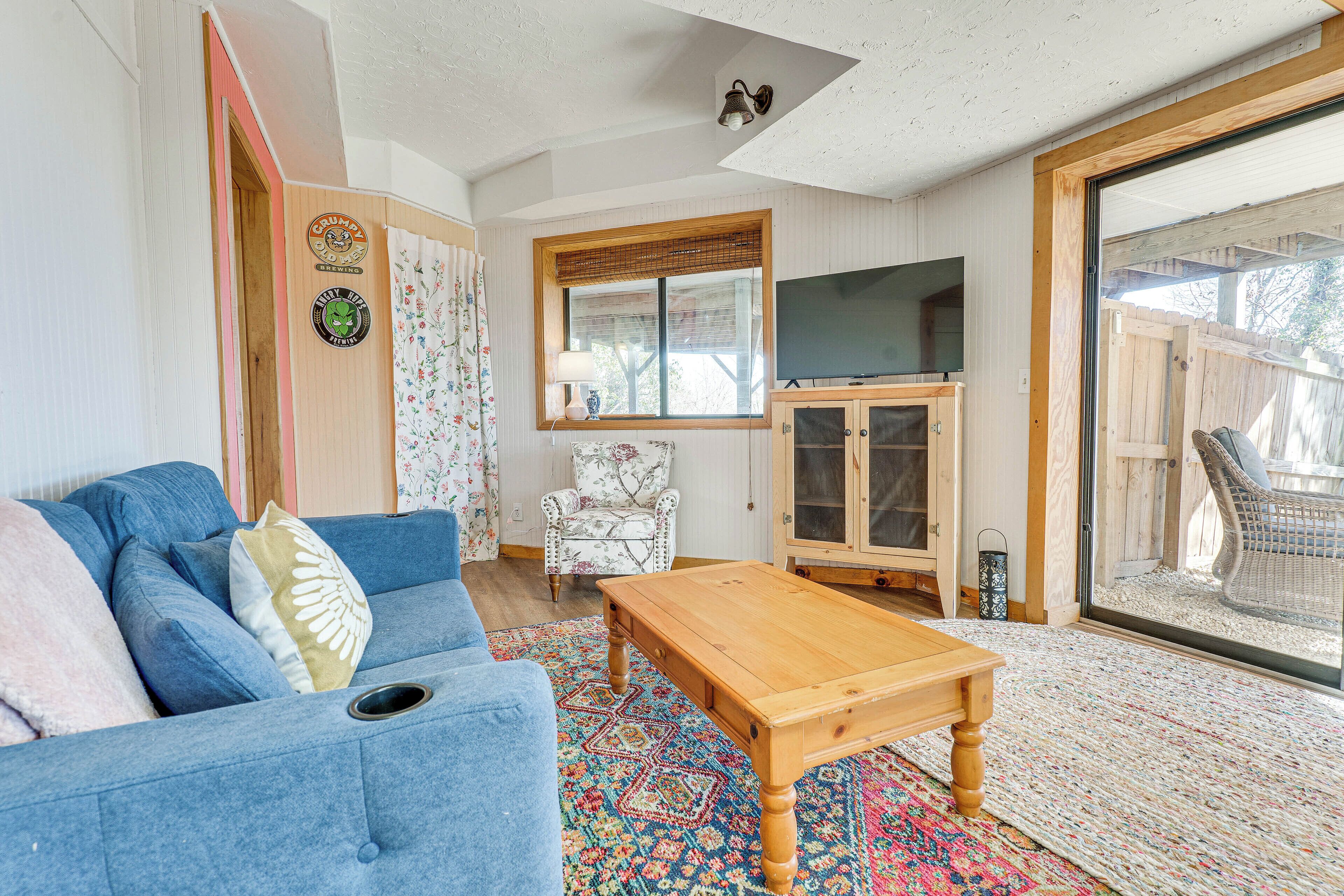 A cozy living room with a blue sofa, a wooden coffee table, a patterned rug, a television, and a wicker chair.