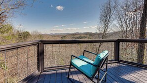 A wooden deck with a metal railing, a single blue cushioned chair, and a view of a mountainous landscape. - Mountaintop Blue Ridge Cabin: 2 Mi to Downtown (Blue Ridge)