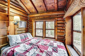 Relax in this cabin room with a large bed and checkered bedspread, surrounded by rustic charm and a forest view.