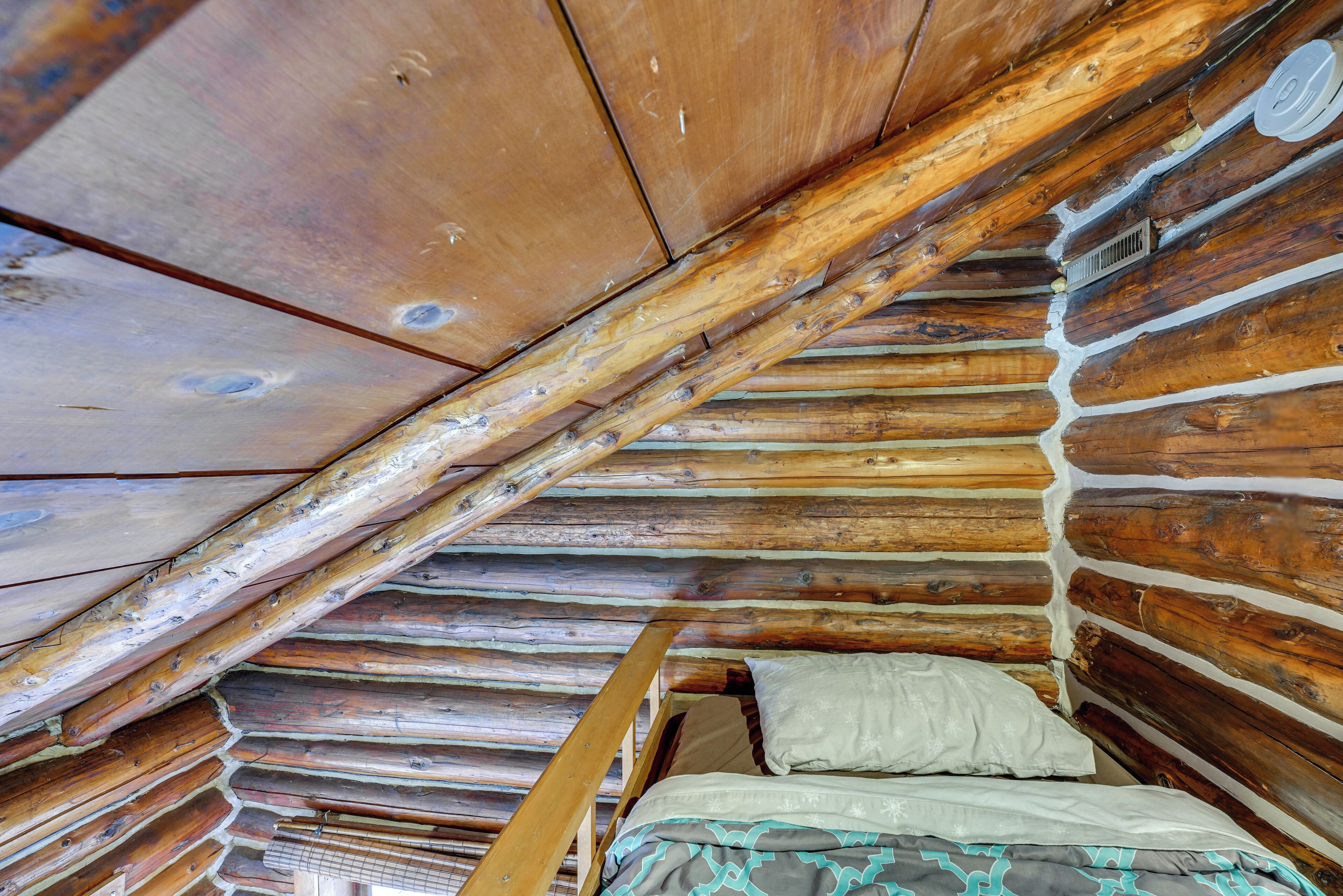 A log cabin bedroom with a loft bed, wooden beams, and a sloped ceiling.