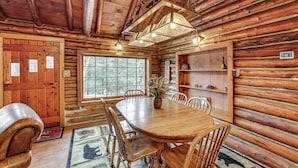 A wooden cabin interior with a dining table, chairs, a chandelier, and a large window.