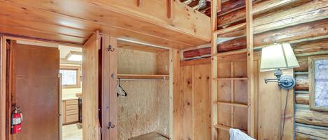 A wooden cabin interior with a bed, a small wooden cabinet, and a closet.