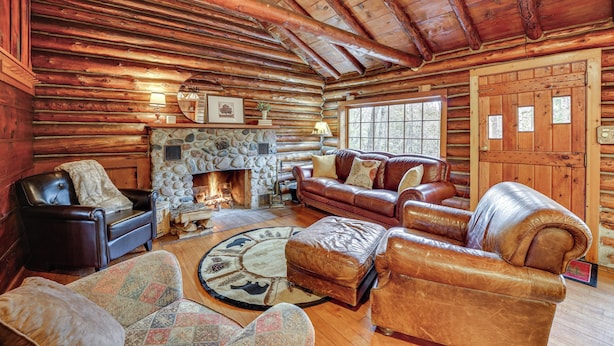 A log cabin interior with a stone fireplace, leather furniture, and wooden walls.