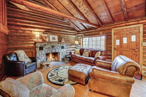 A log cabin interior with a stone fireplace, leather furniture, and wooden walls. - Michigan Log Cabin w/ Pere Marquette River Views (Branch)