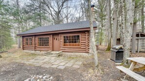 A log cabin with a stone foundation, a fire pit, and a picnic table.