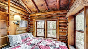 A log cabin bedroom with a bed, a window, and a wall-mounted lamp.