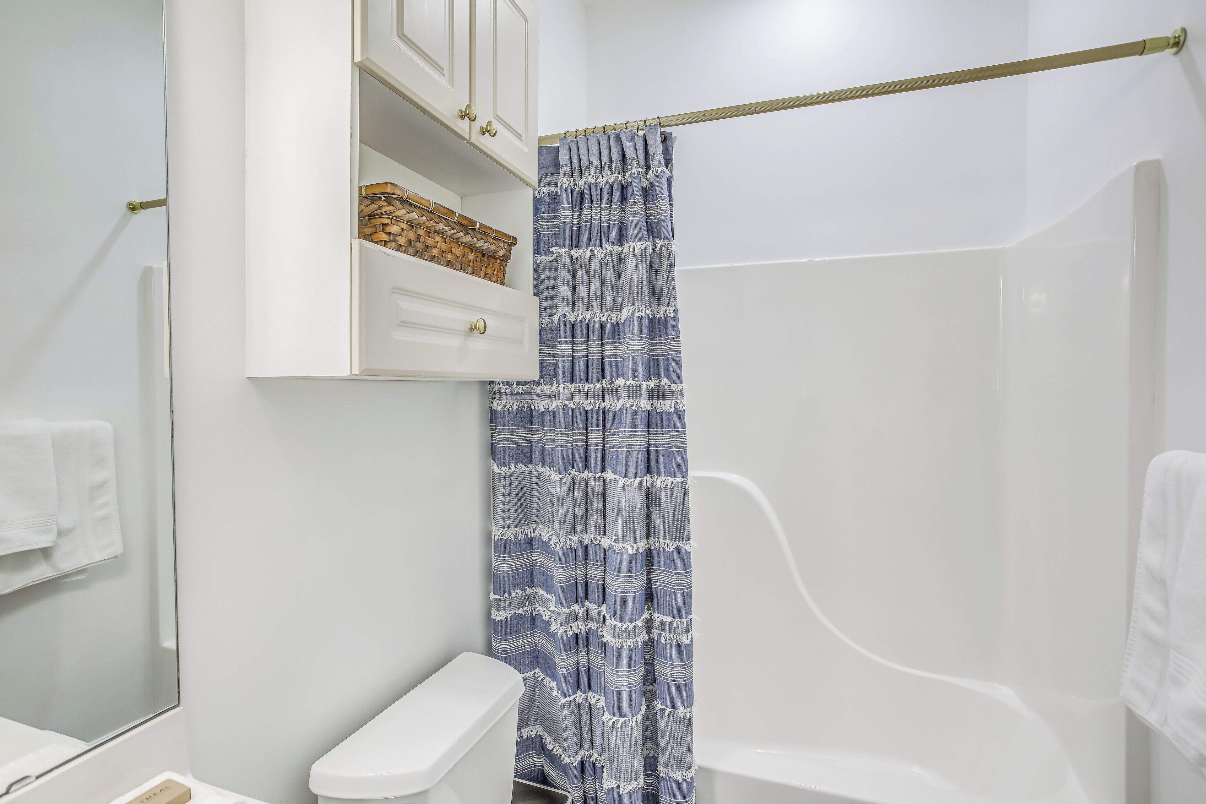 Bagno con un WC bianco, un lavandino bianco, uno specchio, un porta asciugamani e una tenda da doccia.