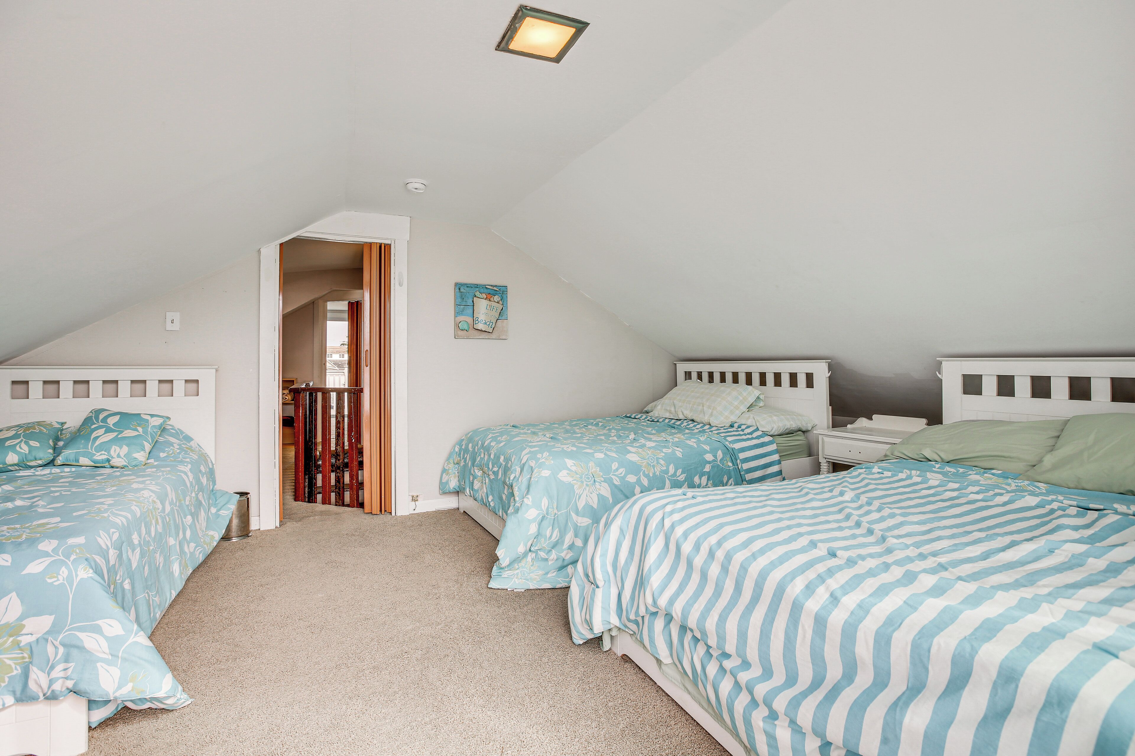 A bedroom with two beds, a small bedside table, a nightstand, and a ceiling light fixture.