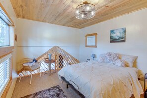 A bedroom with a bed, a chair, a small table, and a painting on the wall. - Cozy & Restful Cabin, Steps to Lake Almanor (Westwood)