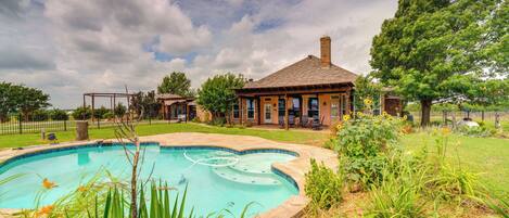 Relax by the pool surrounded by lush greenery and a charming brick building in the background.