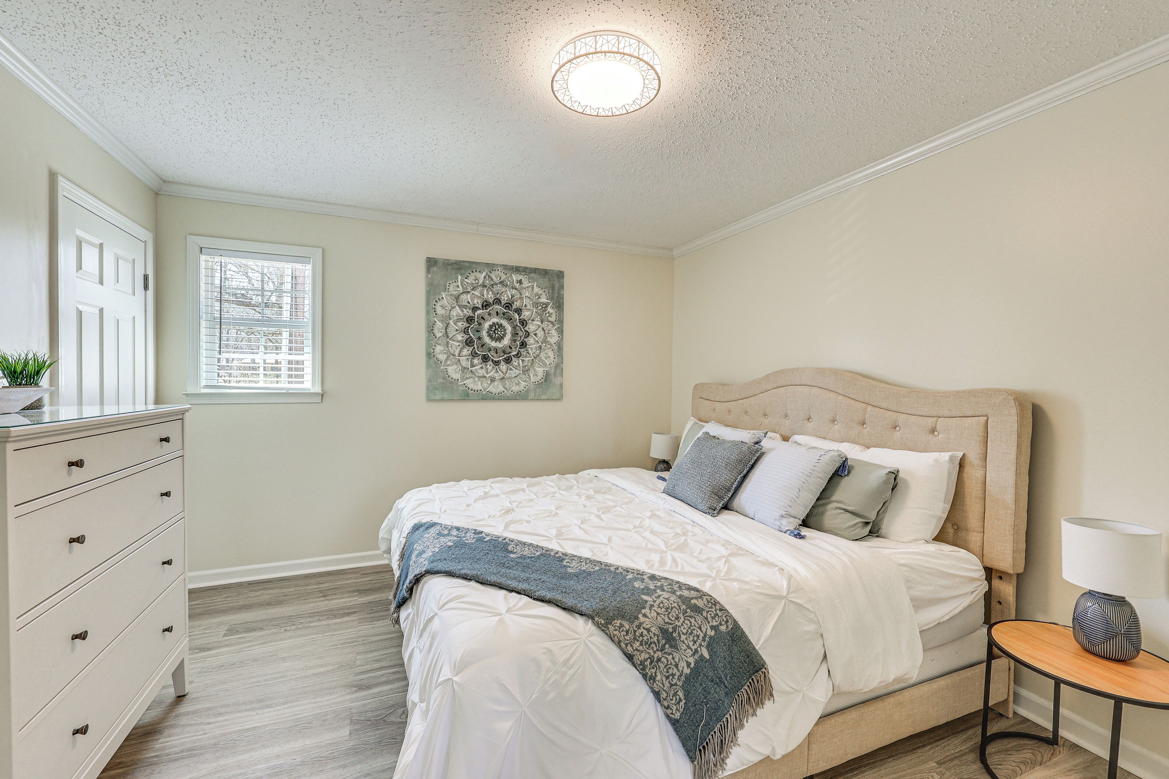A bedroom with a bed, dresser, bedside table, and a wall-mounted artwork.