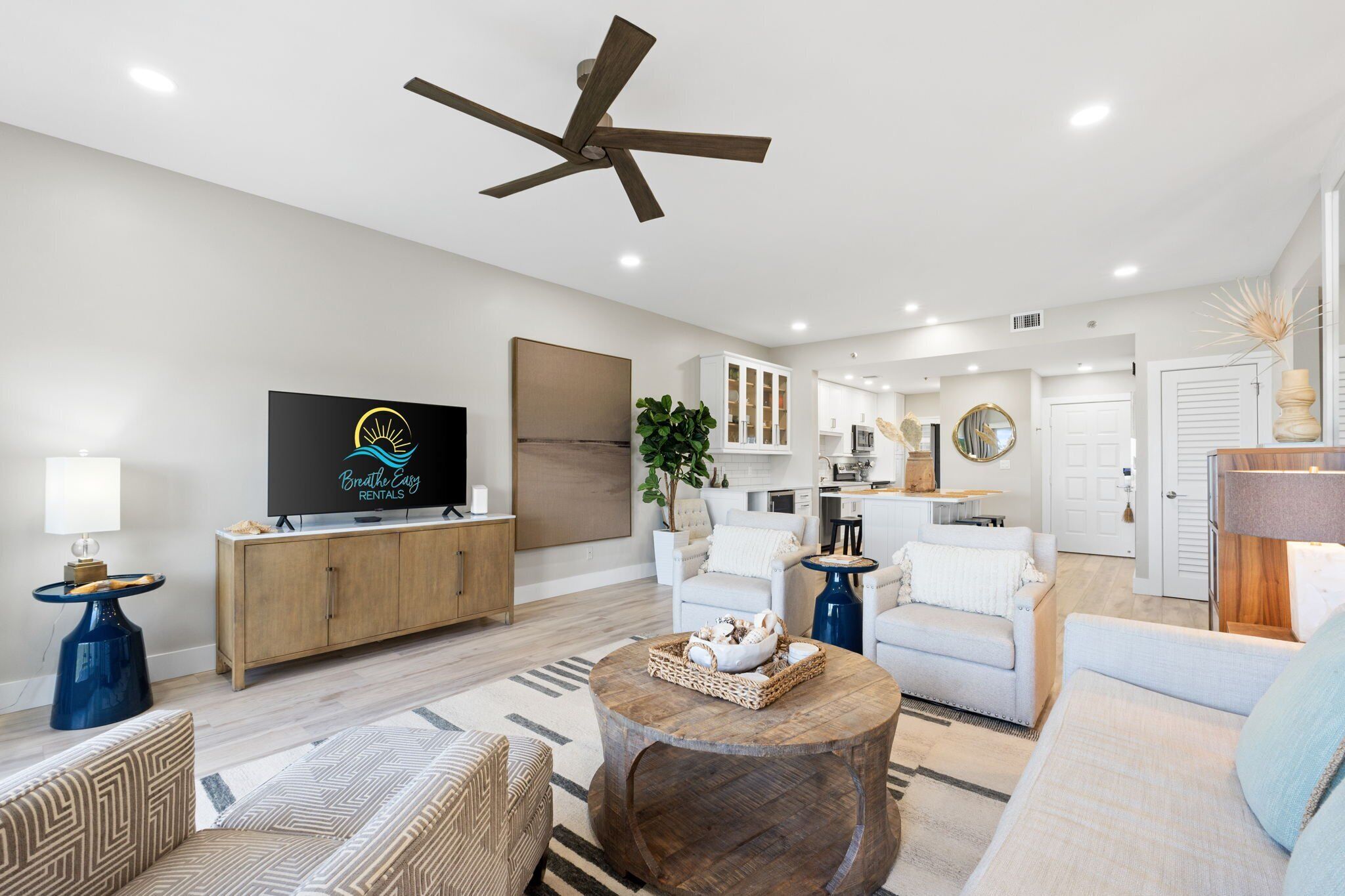 Una sala moderna con ventilador de techo, televisor, aparador de madera, planta y un comedor con mesa y sillas.