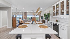 A modern kitchen with a large island, white cabinetry, and a view to the outside. - Shell Seeker - Gulf-View Condo at Tops'l Resort | Pool, Beach Access, Hot Tub, & More! BM 702 (Miramar Beach)