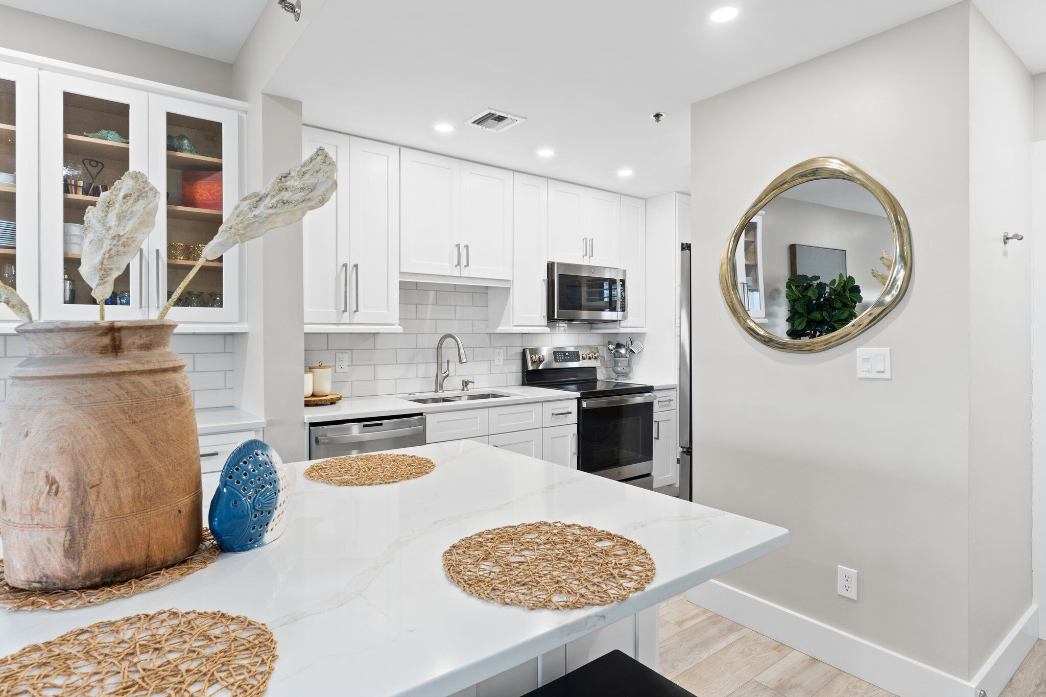 A modern kitchen with white cabinets, a microwave, and a large round mirror.