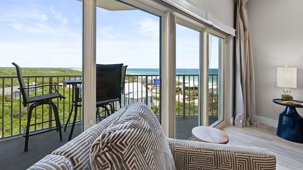 A balcony with a view of the ocean, a sofa, a table, and a lamp. - Shell Seeker - Gulf-View Condo at Tops'l Resort | Pool, Beach Access, Hot Tub, & More! BM 702 (Miramar Beach)