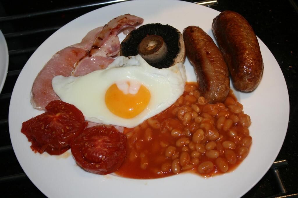 Un plato de comida con tocino, salchichas, huevos, frijoles y tomates.