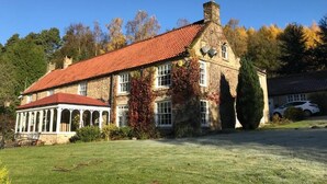 A large stone building with a red-tiled roof, a covered patio area, and a well-maintained lawn. - High Dalby House (Pickering)