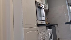 Una cocina con armarios blancos, horno empotrado, lavadora y salpicadero de azulejos.