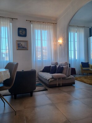 Un salon avec un canapé, des fauteuils, une table et un tableau accroché au mur.