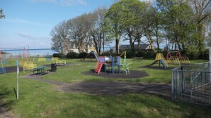 A playground with various play structures, a picnic table, and a fenced area. - Tawelfan (Llwyngwril)