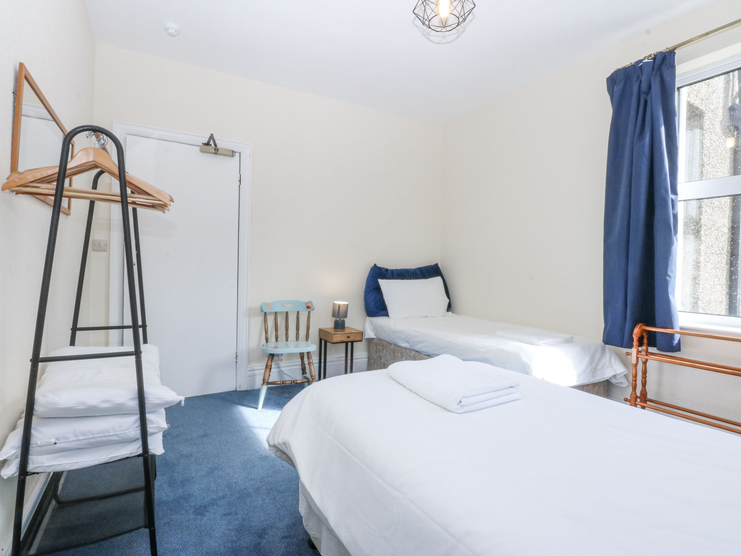 Un dormitorio con dos camas individuales, una escalera de madera, una silla, una mesita y una ventana con cortinas.