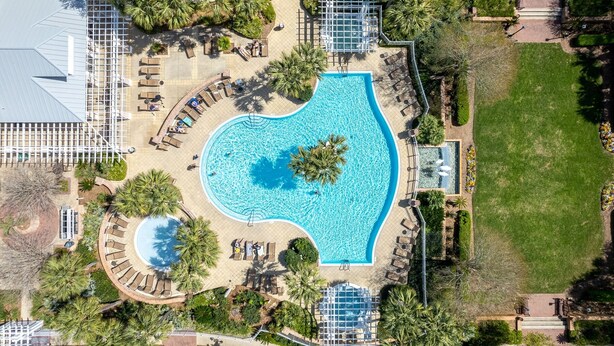 Vista aérea de un complejo turístico con una piscina central, rodeado de zonas de descanso y palmeras.