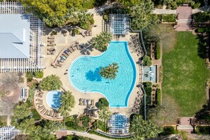 Vista aérea de un complejo turístico con una piscina central, rodeado de zonas de descanso y palmeras.