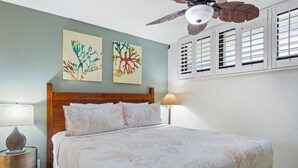 Ein Schlafzimmer mit einem Bett, zwei Wandbildern, einem Deckenventilator und einem Fenster mit Fensterläden.