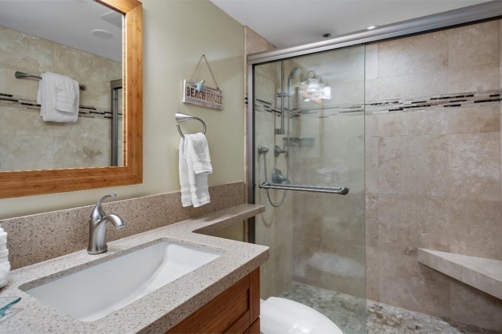 A bathroom with a sink, mirror, towel rack, and a glass-enclosed shower area.
