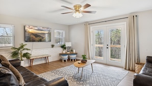 A living room with a ceiling fan, a sofa, a coffee table, and a large window with curtains.