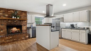 Una cocina moderna con chimenea de ladrillo, armarios blancos y una isla central.
