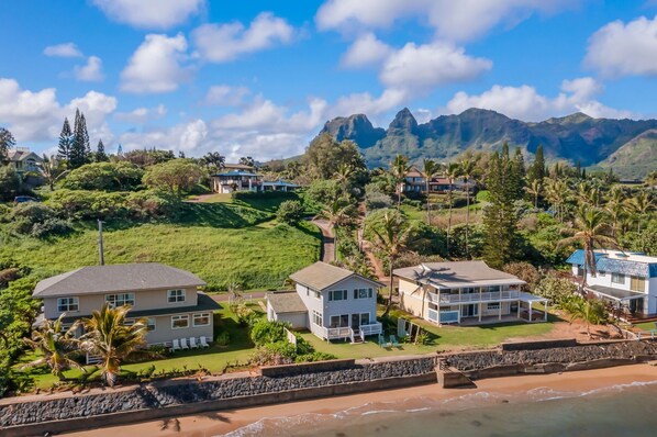 A coastal property with multiple houses, a stone wall, and a beach. - Kauai Aliomanu 2 Bedroom Home (Anahola)
